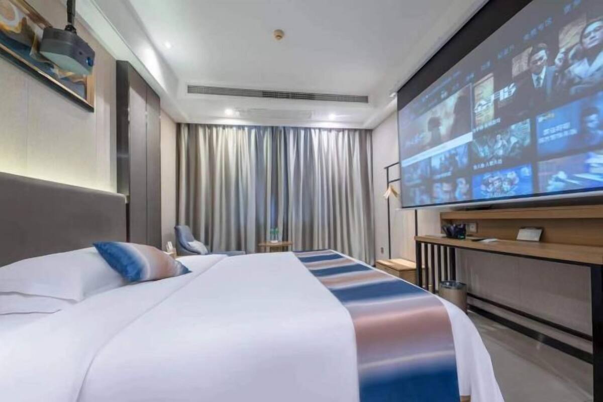 Une chambre d’hôtel comprenant un lit, un écran de télévision diffusant plusieurs chaînes, un bureau avec une chaise et un rideau.