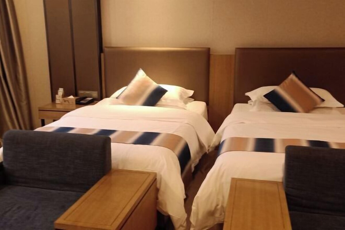 A hotel room with two beds, each with a headboard, a bedside table, and a chair.