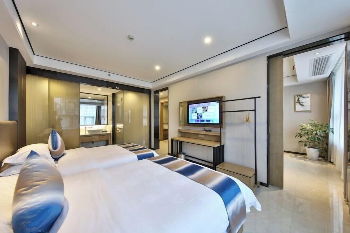 A modern hotel room with a large bed, a television, a mirror, and a small desk.
