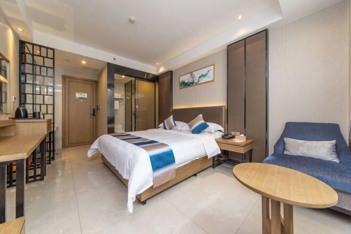 A modern hotel room with a bed, a desk, a chair, and a sofa.