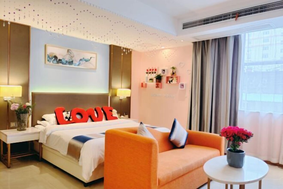 A hotel room with a bed, a sofa, a small table with a vase, and a wall with a picture and decorations.