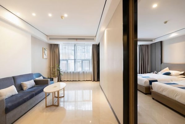 A modern hotel room with a sofa, a small table, two beds, and a large window with curtains.