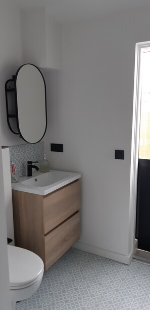 Un baño pequeño con lavamanos blanco, un espejo, inodoro y baldosas de piso con diseño.