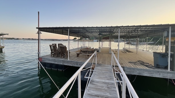 Une jetée en bois mène à un espace de repos abrité, équipé de chaises et d’une table, et d’où l’on peut admirer une étendue d’eau calme.