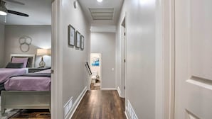 Ein schmaler Flur mit einem Bett links, einem Deckenventilator und einer Tür am Ende.
