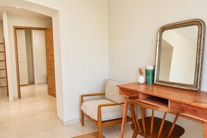 Une pièce comprenant un bureau en bois, une chaise, un grand miroir et une porte donnant sur une autre pièce.