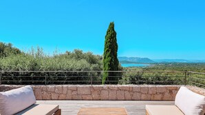 An outdoor seating area with a stone wall, wooden furniture, and a view of a coastal landscape. - Villa Casta Joia Di Cirendinu (Sainte Lucie de Porto-Vecchio)