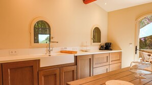 A kitchen with wooden cabinets, a white countertop, and a wooden dining table. - Villa Casta Joia Di Cirendinu (Sainte Lucie de Porto-Vecchio)