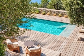 Une terrasse en bois avec une piscine, entourée de verdure et de murs en pierre.