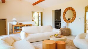A spacious living room with white sofas, wooden beams on the ceiling, a wooden cabinet with glass doors, a round mirror, and a small round table with a lamp. - Villa Casta Joia Di Cirendinu (Sainte Lucie de Porto-Vecchio)