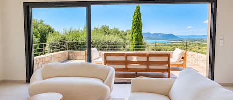 Un balcón con sofá y sillones, una mesa de madera y vistas a zonas verdes y montañas.