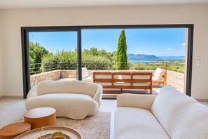 Un balcon avec un canapé et des fauteuils, une table en bois, et une vue sur la verdure et les montagnes.