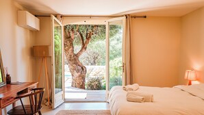 A bedroom with a bed, a desk, a chair, and a view of a tree through an open door. - Villa Casta Joia Di Cirendinu (Sainte Lucie de Porto-Vecchio)