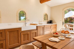 Une cuisine avec des meubles en bois, un plan de travail blanc et un coin repas où une table est dressée pour le petit-déjeuner.