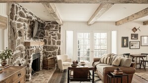 Un salon chaleureux avec une cheminée en pierre, des meubles en bois et une grande fenêtre donnant sur l’extérieur.