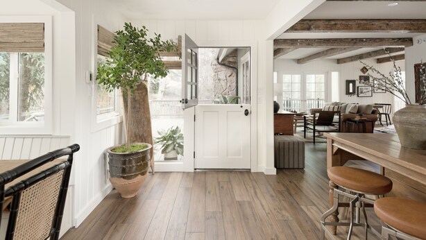 Une cuisine spacieuse avec un plancher en bois, un coin repas avec une table en bois et des tabourets de bar, et une vue sur l’extérieur par une porte.