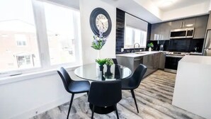 A modern kitchen with stainless steel appliances, a round dining table with chairs, and a large window providing a view of the outside. - Cozy 2BR Suite with Parking and 5 min Drive To Falls Sleeps 6! (Niagara Falls)