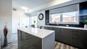 A modern kitchen with a central island, dark cabinetry, and a large window providing natural light. - Cozy 2BR Suite with Parking and 5 min Drive To Falls Sleeps 6! (Niagara Falls)