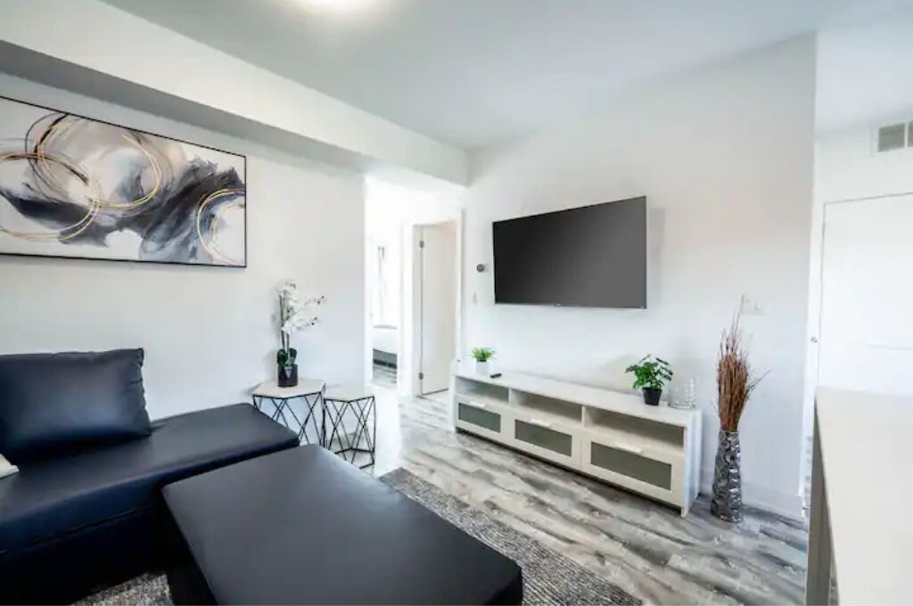 Un salon moderne avec un canapé noir, un meuble de rangement blanc et un grand tableau abstrait accroché au mur.