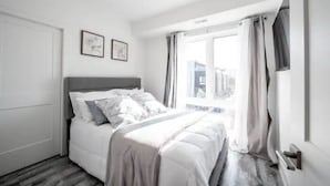 A bedroom with a bed, a window with curtains, and two framed pictures on the wall. - Cozy 2BR Suite with Parking and 5 min Drive To Falls Sleeps 6! (Niagara Falls)