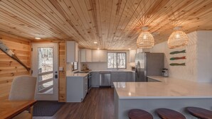 Eine moderne Küche mit Holzwänden, einer zentralen Kochinsel, Barhocker und Blick ins Freie.