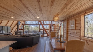 Ein gemütliches Blockhaus-Interieur mit Holzbalkendecke, einer Couch, einem Esstisch und einem Kamin.
