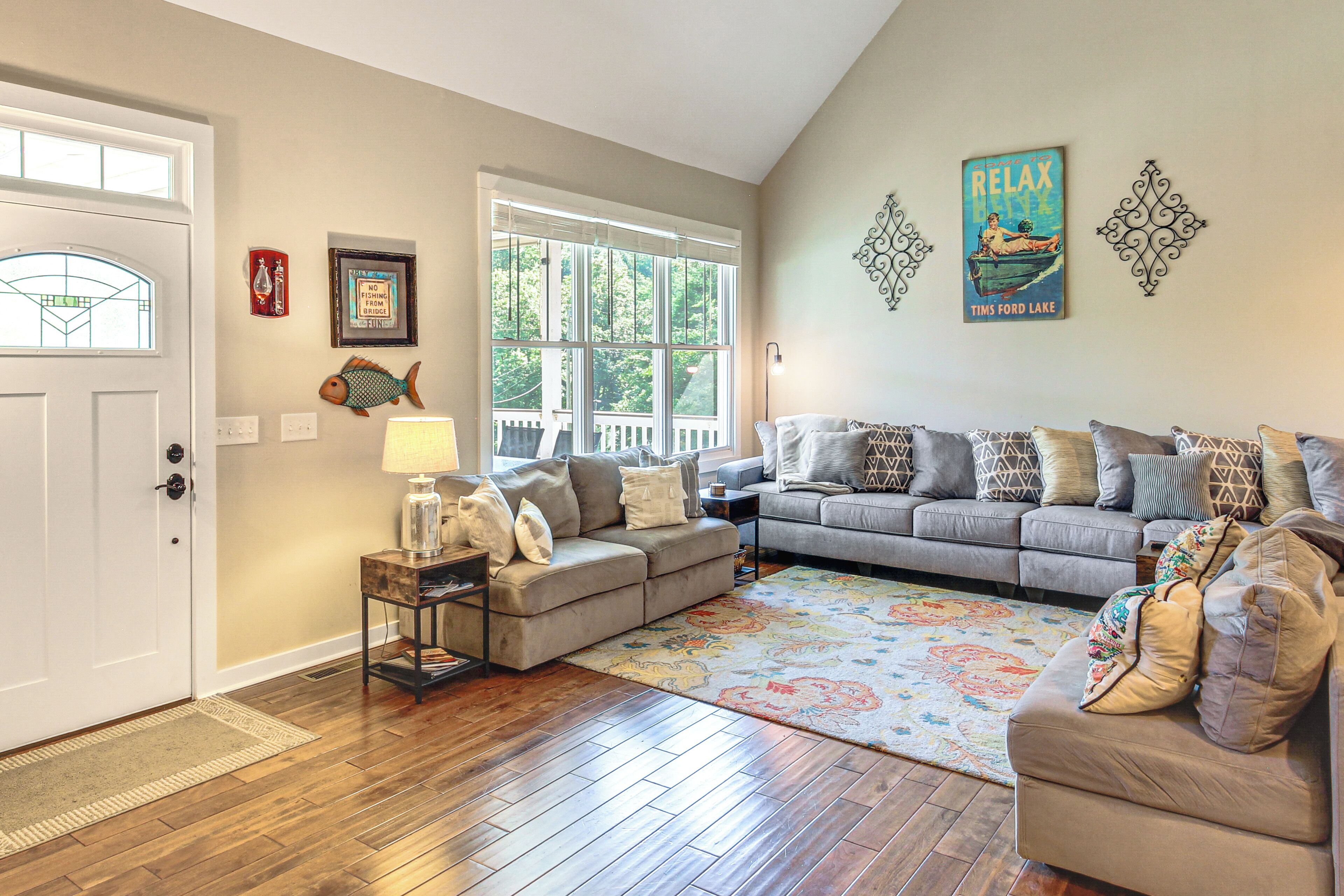 A living room with a sofa, a coffee table, and a rug. There is a door with a window, and a wall with decorative items.
