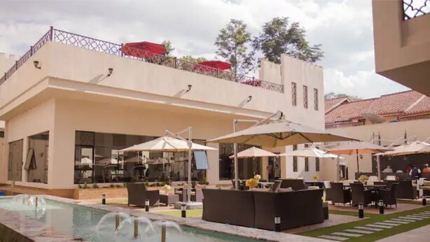 Un espace piscine avec des chaises longues et des parasols, une fontaine et un bâtiment doté d’un balcon.