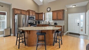 A spacious kitchen with wooden cabinets, a stainless steel refrigerator, a microwave, and a large island with stools. - Hot Tub + Arcade -> Memorable Stay
 (Hollister)