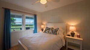 A bedroom with a bed, two bedside lamps, a nightstand, a ceiling fan, and a window with curtains. - Beachfront Vacation Rental with AC throughout (Hanalei)