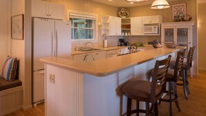 A modern kitchen with a central island, bar stools, and pendant lighting. - Beachfront Vacation Rental with AC throughout (Hanalei)