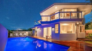 Una casa moderna de dos pisos con piscina, ventanas amplias y un balcón.