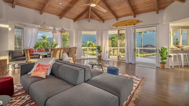 Amplia sala de estar con techo alto de madera, un sofá gris y una zona de comedor con vistas al exterior.