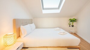 A modern bedroom with a skylight, a bed, a bedside lamp, and a small table with plants. - GuestReady - Sunny spacious in Belém (Lisbon)