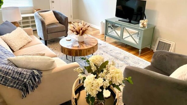 A living room with a sofa, armchairs, a coffee table, a TV on a cabinet, and a door in the background. - Dogtown St Louis Family & Pet Favorite!Yard, Barnes, SLU,WashU, Forest Park,Zoo (St. Louis)