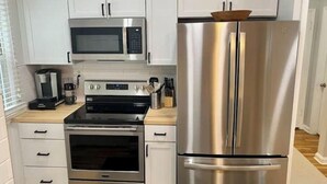 A modern kitchen with white cabinets, a stainless steel refrigerator, a microwave, a stove, and a coffee maker. - Dogtown St Louis Family & Pet Favorite!Yard, Barnes, SLU,WashU, Forest Park,Zoo (St. Louis)
