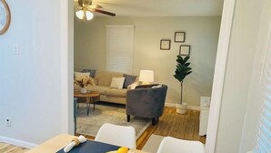 A dining area with a table set for two, a bowl of lemons, and a view into a living room with a sofa, a lamp, and a plant. - Dogtown St Louis Family & Pet Favorite!Yard, Barnes, SLU,WashU, Forest Park,Zoo (St. Louis)