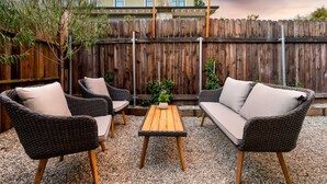 A patio area with wicker furniture and a wooden table, surrounded by a wooden fence and a building in the background. - Designer Digs (Monrovia)