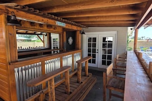 A wooden outdoor seating area with a dartboard, a sign, and a door leading to an adjacent building.
