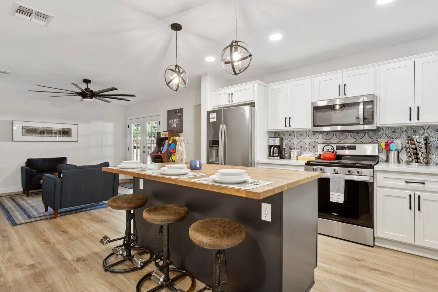 A modern kitchen with a central island, bar stools, a ceiling fan, and a microwave.