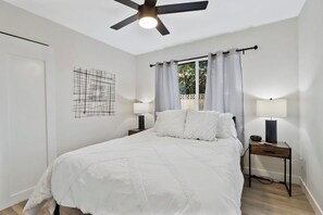 A bedroom with a bed, two bedside tables with lamps, a ceiling fan, and a window with curtains.