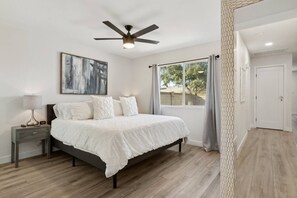 A bedroom with a bed, nightstand, lamp, ceiling fan, and a window with curtains.