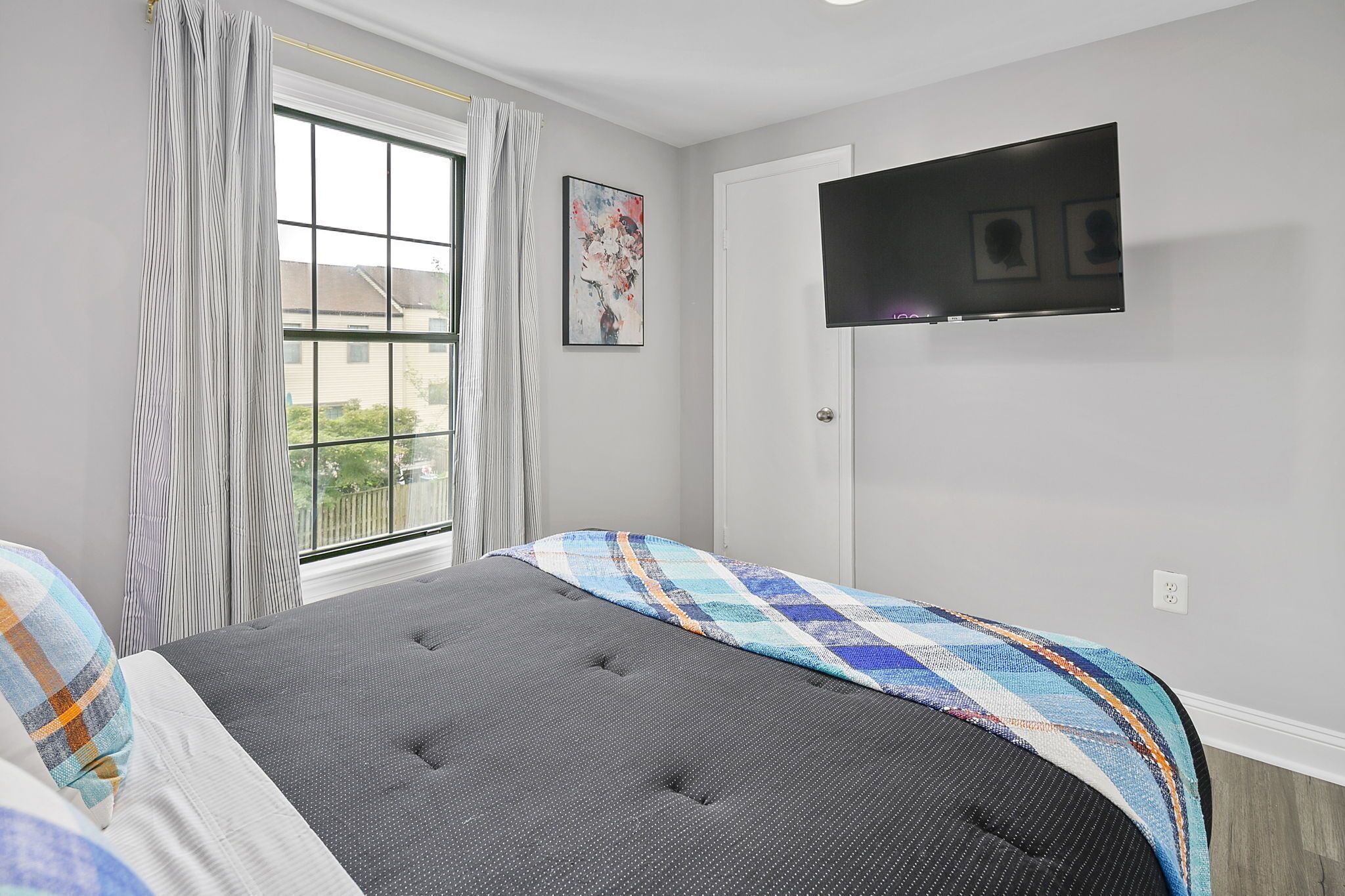 Een slaapkamer met een bed, een raam met gordijnen, een flatscreentelevisie aan de muur en een schilderij.