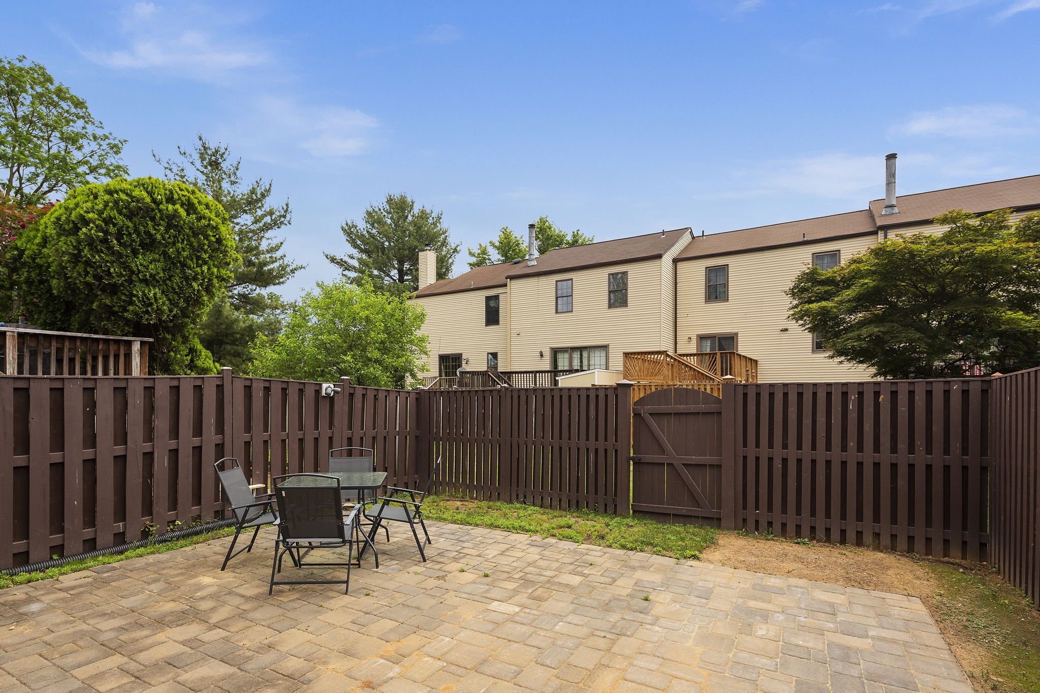 A backyard with a patio area, a wooden fence, and a view of a two-story building.