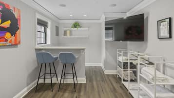 Une chambre compacte et moderne, dotée d’une kitchenette, de deux tabourets de bar, d’une télévision et d’une étagère où sont pliés les serviettes.