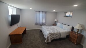 A bedroom with a bed, a desk, a TV, and a window with curtains.