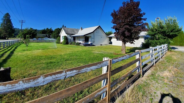 A rural property with a white house, a wooden fence, and a grassy field.