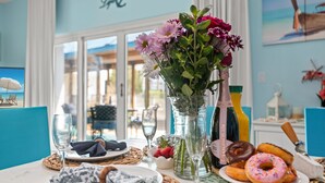 A dining table with a vase of flowers, a bottle of champagne, and a plate of donuts. - 3101 Spring Special Discount Book Mar 6th ~Poolside ~Heated Pool ~Hot Tub (Destin)