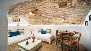 Una habitación acogedora con techo de piedra, una cama, un sofá, una mesa de comedor con sillas y una mesa auxiliar.