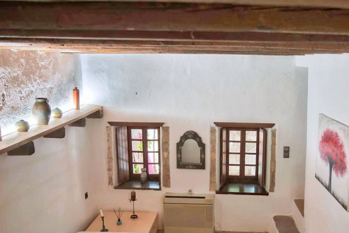 Ein kleiner, gemütlicher Raum mit zwei Betten, einem Holzregal mit Dekorationen, einem Spiegel und einem Fenster mit Blick.